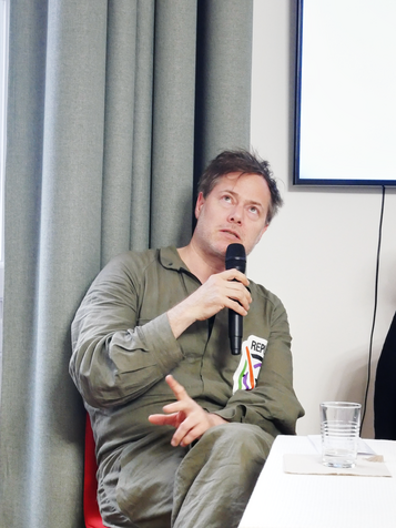 Milo Rau mit Mikrofon am Podium